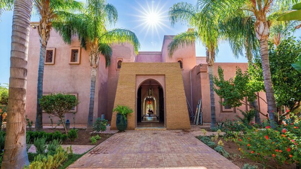 A courtyard with a brick pathway leading to a building entrance, surrounded by palm trees and a garden. - Luxury villa with swimming pool, not overlooked. (Marrakech)