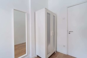 Quarto com guarda-roupa branco, porta e espelho.