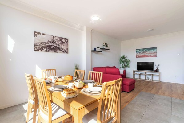 Un coin repas avec une table et des chaises en bois, un canapé rouge et un meuble pour la télévision avec un écran plat.