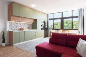 Une cuisine moderne avec des meubles de couleur verte, un canapé rouge et un coin repas offrant une vue sur les arbres.