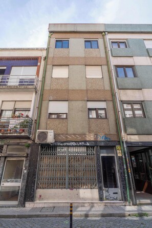 Un immeuble à plusieurs étages doté d’une entrée sécurisée par un portail, de balcons ornés de plantes en pot et d’un appareil de climatisation visible.