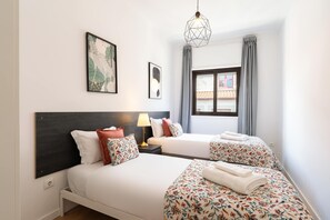 Une chambre d’hôtel avec un lit, une table de chevet, une lampe, une fenêtre avec des rideaux et des œuvres d’art accrochées au mur.