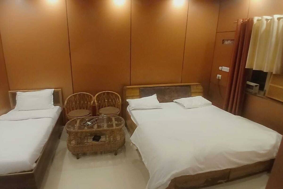 Une chambre d’hôtel avec deux lits simples, une petite table, deux chaises en osier et une tête de lit en bois.