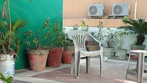 A courtyard with potted plants, a white plastic chair, and an air conditioning unit on a building wall. - Shiv Ganga Hotel (Narendranagar)