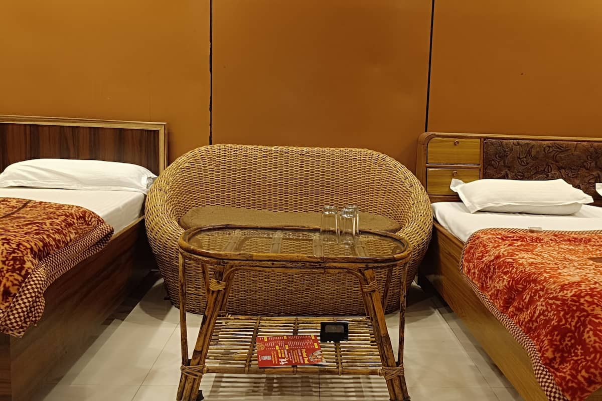 Une chambre d’hôtel avec deux lits simples, un canapé en osier et une petite table avec un plateau en verre.