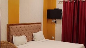 A hotel room with a large bed, a flat-screen TV, a ceiling fan, and a red curtain. - Shiv Ganga Hotel (Narendranagar)
