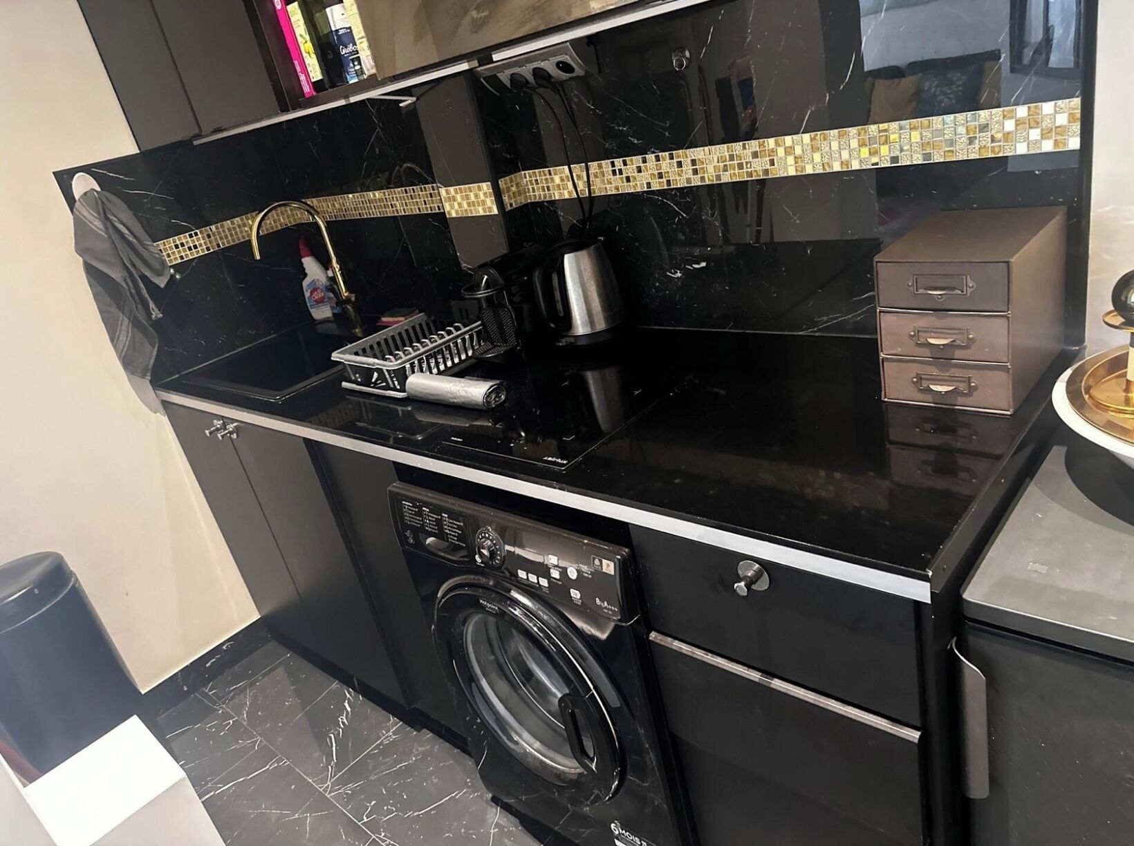 A compact kitchen with a black countertop, a washing machine, and a small cabinet.