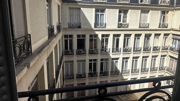 A multi-story building with balconies and windows, viewed from a balcony with a metal railing. - Charment T2 Champ-Elysée    (Paris)