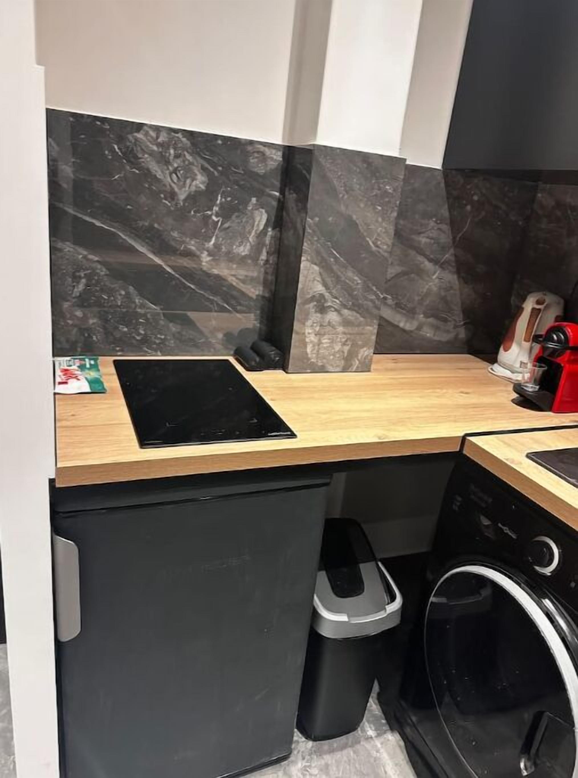 Eine kleine Küche mit einer Holzauskładung, einem schwarzen Geschirrspüler, einem Mülleimer und einer roten Kaffeemaschine.