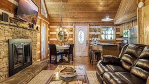 A cozy interior with a stone fireplace, leather sofa, dining area, and kitchen. - Sneaky Bear Getaway, Hot Tub, WIFI,  $560 FREE tickets each paid day!!! (Sevierville)