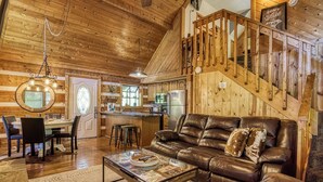 A cozy living room with a leather sofa, a glass coffee table, and a dining area with a wooden table and chairs. A kitchen with modern appliances is visible in the background. - Sneaky Bear Getaway, Hot Tub, WIFI,  $560 FREE tickets each paid day!!! (Sevierville)