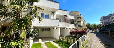 A residential building with multiple balconies, a paved pathway, and lush greenery.