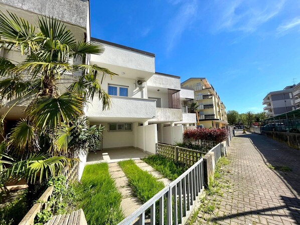 A residential building with multiple balconies, a paved pathway, and lush greenery.