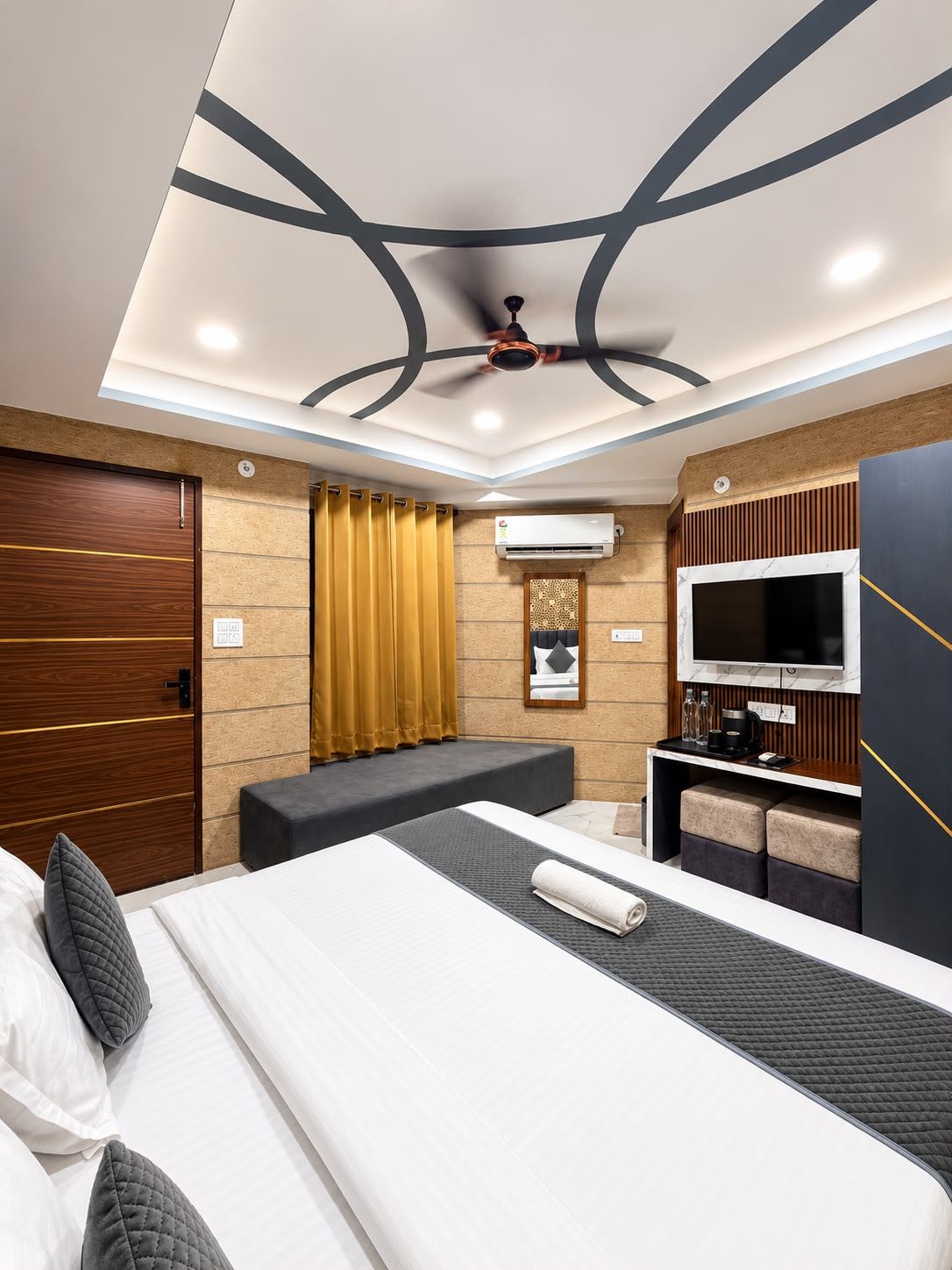 A modern hotel room with a large bed, a seating area, a TV, and an air conditioning unit.