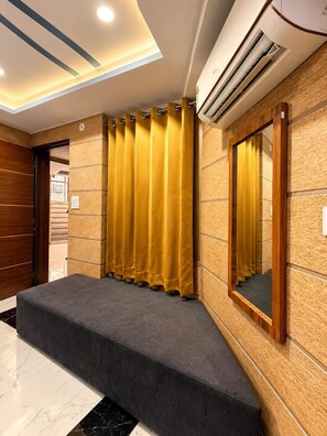 A hotel lobby with a marble floor, a grey carpeted area, a wooden door, and a wall-mounted air conditioner. - Hotel Asha Delight (Narendranagar)