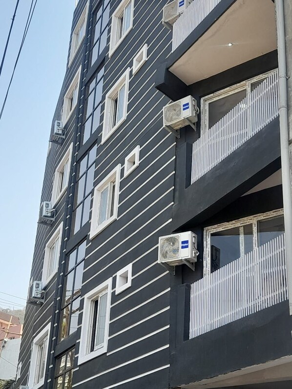 Un immeuble à plusieurs étages, doté de climatiseurs installés à l’extérieur, de balcons avec des garde-corps et surplombant un ciel dégagé.