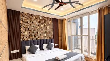 Una habitación de hotel moderna con una cama grande, un ventilador de techo y vistas al exterior a través de un amplio ventanal.
