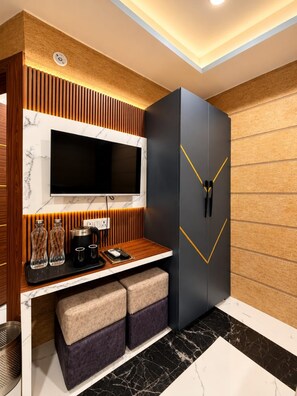 A modern living room with a flat-screen TV, a dark-colored cabinet with a geometric design, and a wooden accent wall. - Hotel Asha Delight (Narendranagar)