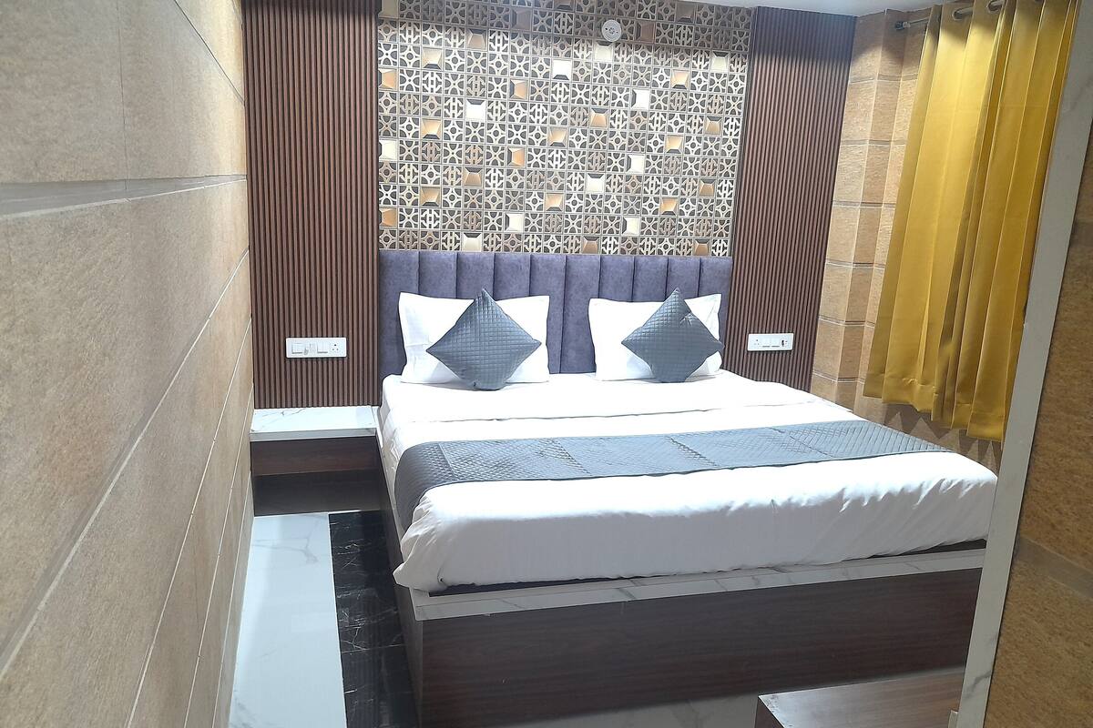 A modern bedroom with a patterned wall, a dark headboard, and a bed with white bedding and two pillows.