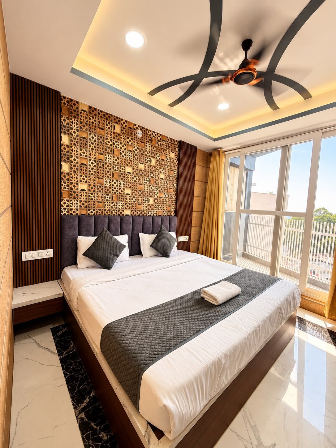 Habitación de hotel con una cama grande, ventilador de techo, panel decorativo en la pared y vista por la ventana.