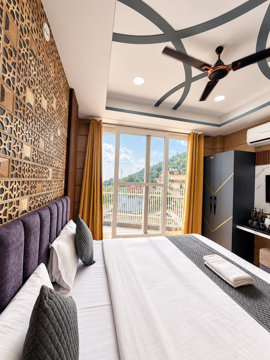 A hotel room with a large bed, a ceiling fan, a view of the outdoors, and a minibar.