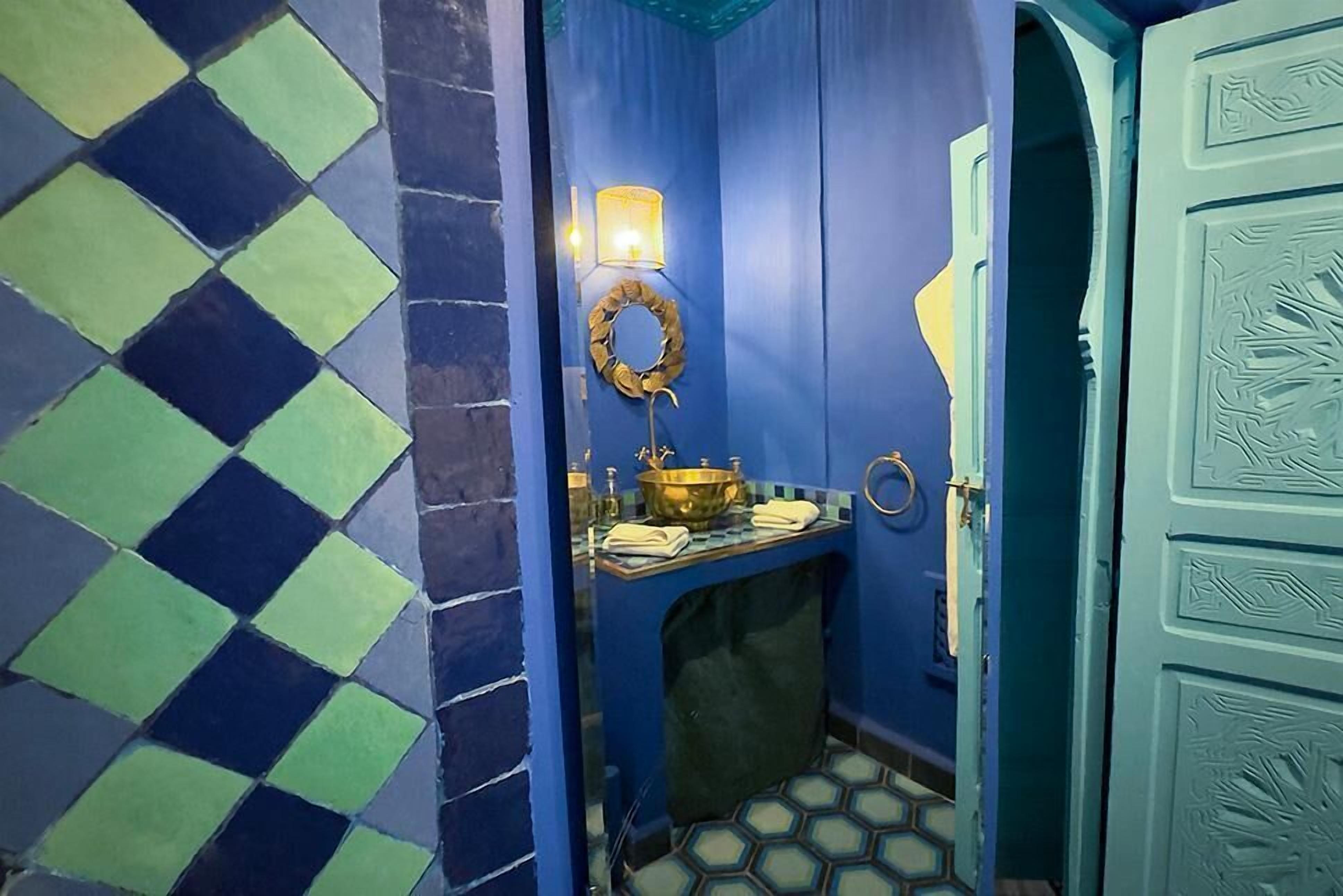 A bathroom with a blue and green checkered floor, a sink with a gold basin, and a wall-mounted light fixture.