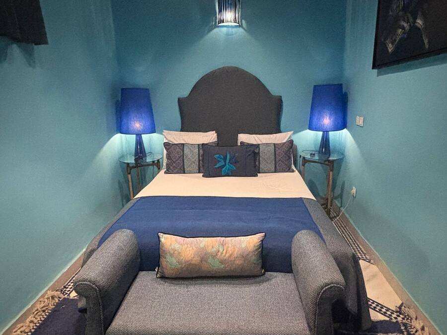Une chambre à coucher comprenant un lit, deux tables de chevet avec des lampes, un banc au pied du lit et un luminaire fixé au mur.