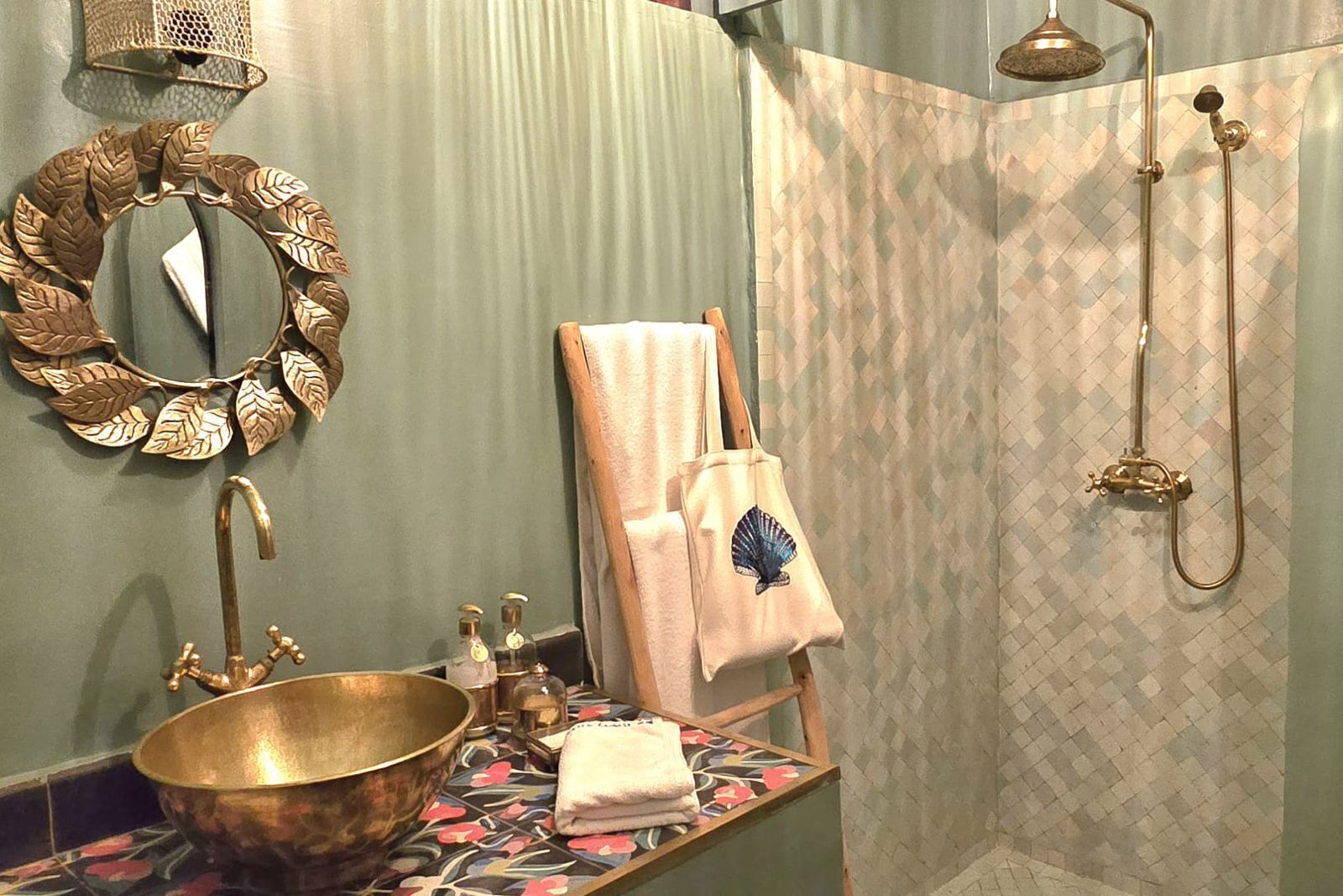 Un baño con un lavamanos grande dorado, un espejo decorativo, un perchero para toallas y una zona de ducha.