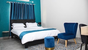 A modern bedroom with a bed, a blue chair, and a small table. - Ascentia Guest House (Jwaneng)