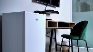 A modern room with a white mini-fridge, a wooden desk with a flat-screen TV, and a green chair. - Ascentia Guest House (Jwaneng)