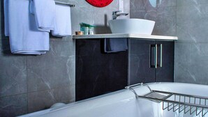 A modern bathroom with a bathtub, a round mirror, and a vanity with a sink. - Ascentia Guest House (Jwaneng)