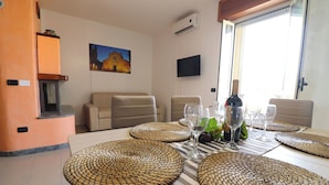 Een eetruimte met een tafel voor zes personen, omringd door beige banken, een televisie aan de muur en een schilderij boven de banken.