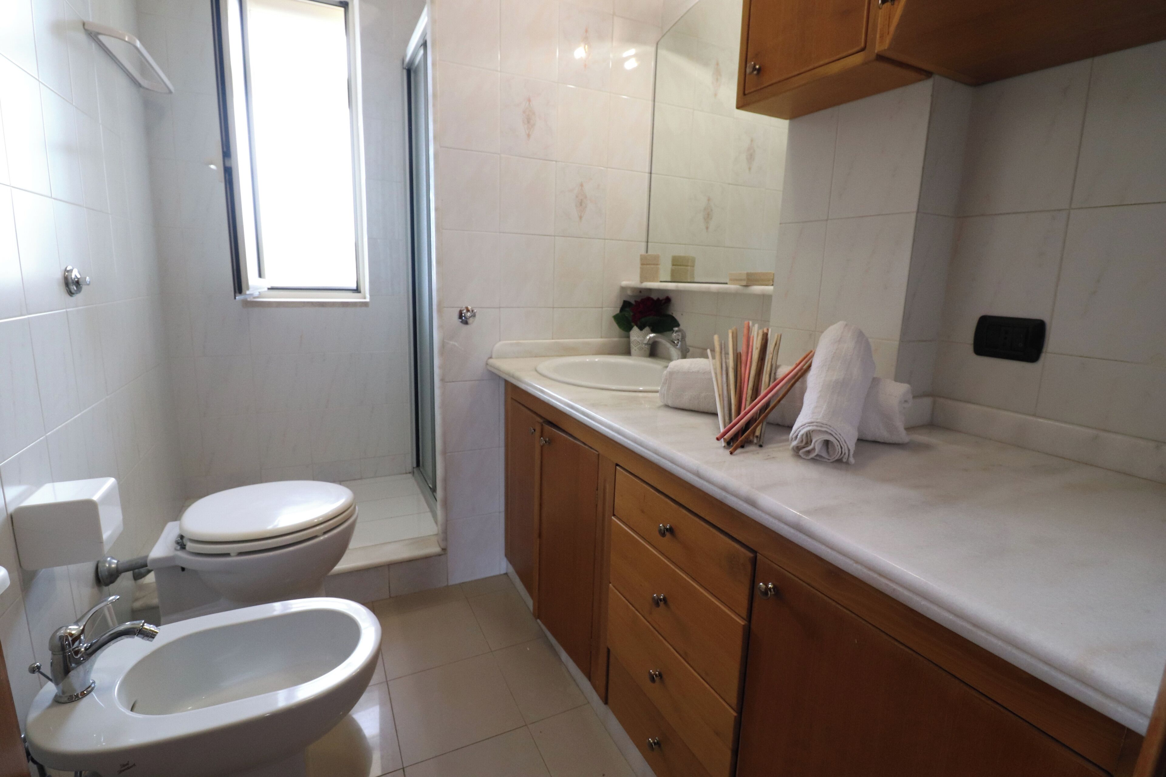 Ein Badezimmer mit Toilette, Bidet, Waschbecken, Holzschrank und Fenster.