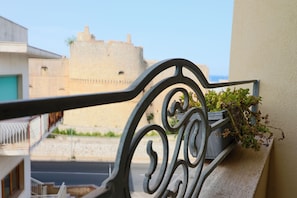 A balcony with a wrought iron railing, a potted plant, and a view of a historic stone building in the background. - Calipso's Home in Otranto (Otranto)