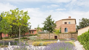 A garden with lavender and other plants, a stone wall, and a brick building with a window and door. - Cignella Resort (Trequanda)
