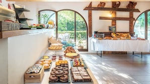 A buffet with various desserts and pastries, a wooden ceiling, and a view of greenery through large windows. - Cignella Resort (Trequanda)