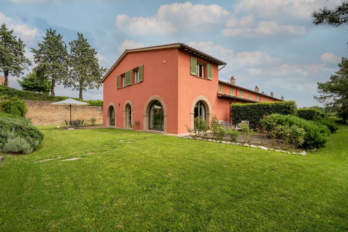 A two-story house with a red facade, green shutters, and a well-maintained lawn.