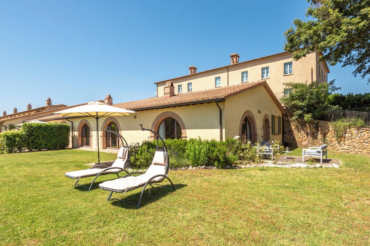 A building with a large lawn area, two lounge chairs, and a patio umbrella.
