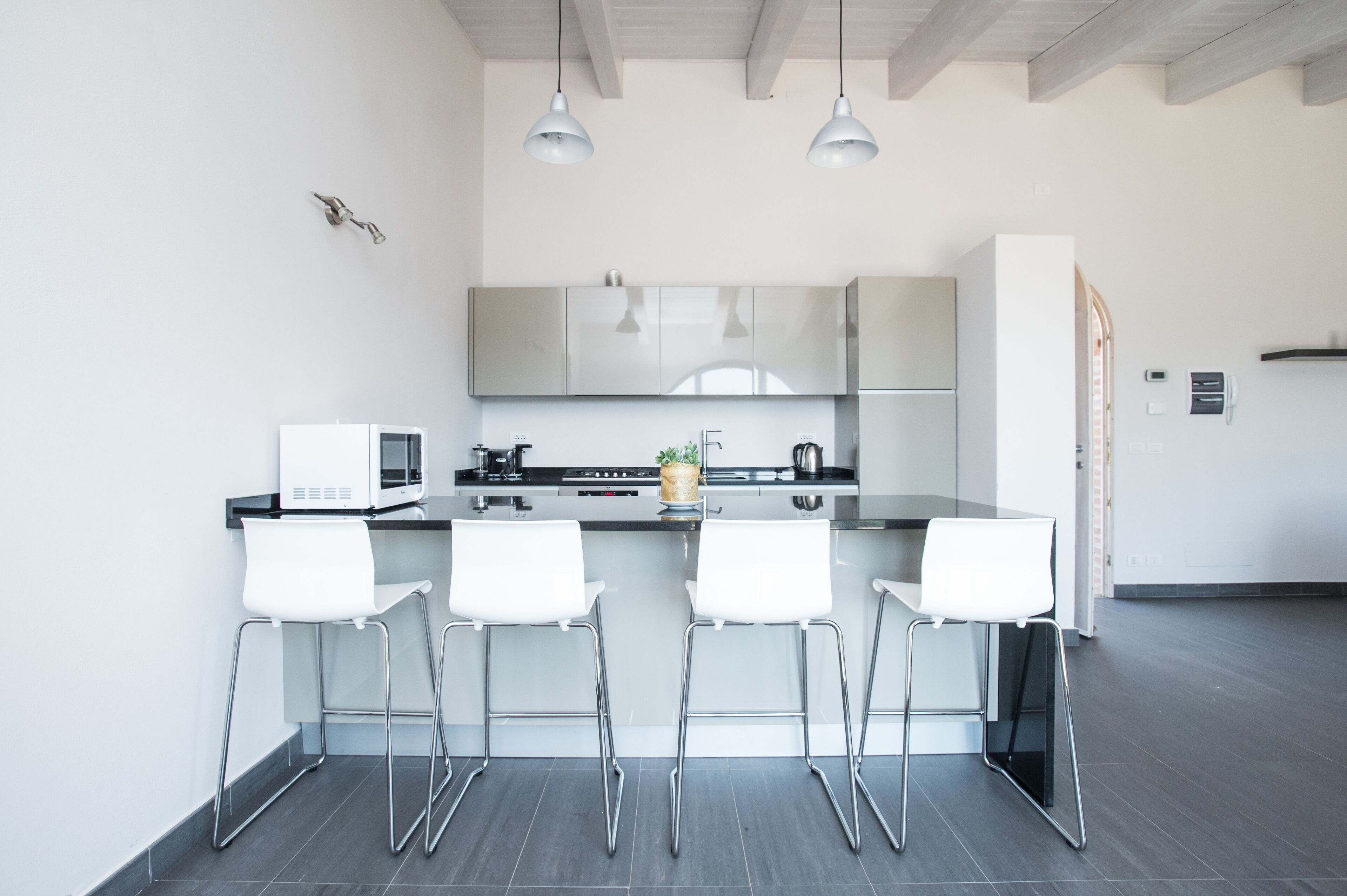 A modern kitchen with white cabinets, a black countertop, and three white bar stools.