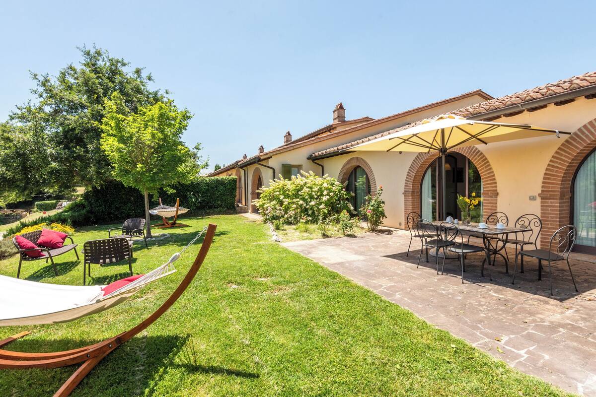 A patio area with a hammock, outdoor seating, and a table under an umbrella.