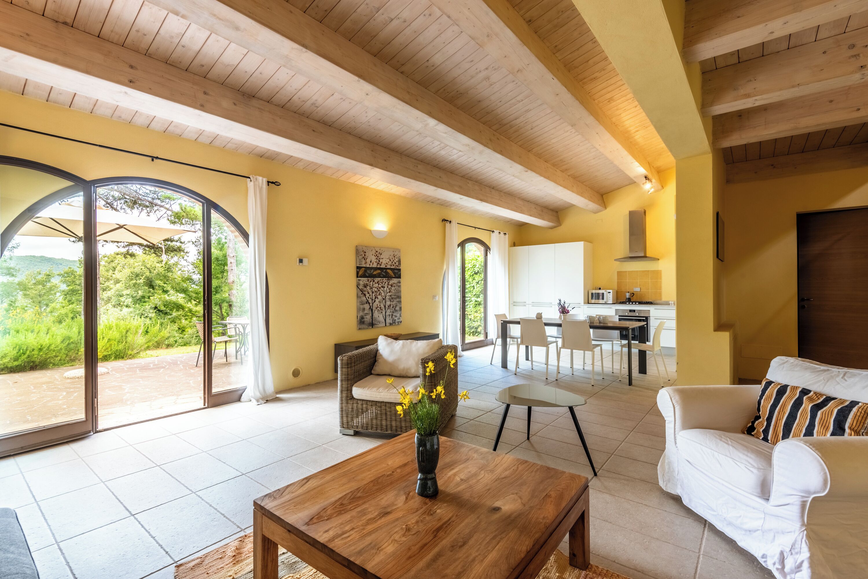 Ein großzügiger Wohnbereich mit einem Holztisch, einem weißen Sofa und einem Esstisch mit Stühlen. Große Glasschübe führen zu einer Terrasse mit Blick ins Grüne.