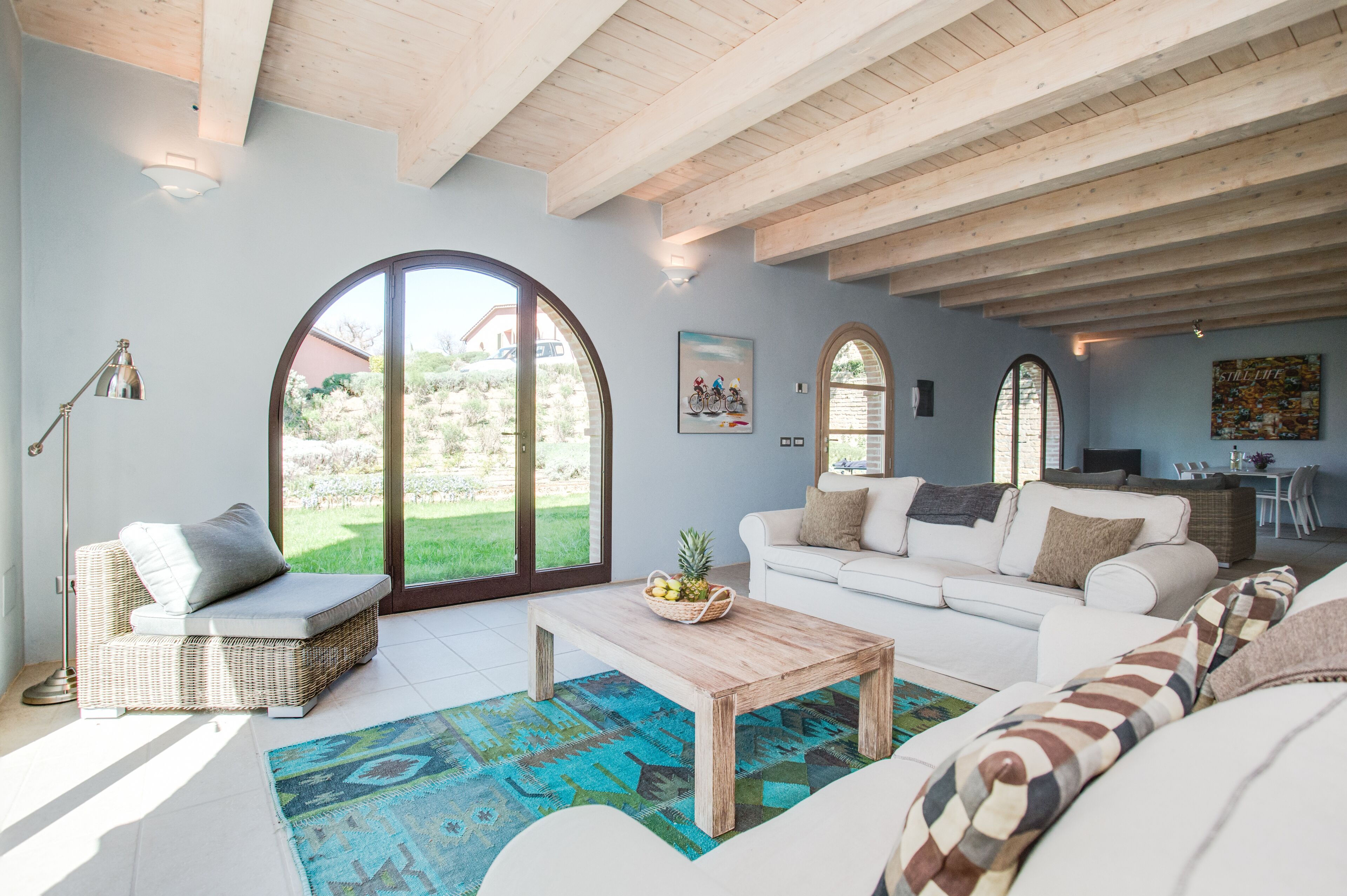 A spacious living room with a large window, a white sofa, a wooden coffee table, and a wicker chair.