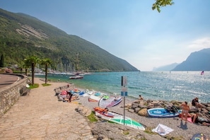 A coastal area with a stone pathway leading to a beach with boats and a mountainous backdrop. - Villa Schlosser Lake Front & Private Pool (Malcesine)
