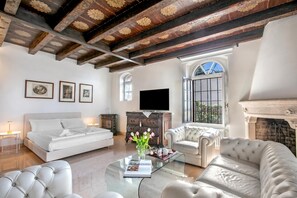 A spacious room with a bed, a sofa, a coffee table with a book and flowers, a fireplace, and a TV. - Villa Schlosser Lake Front & Private Pool (Malcesine)