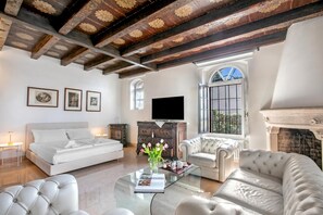 Une pièce spacieuse comprenant un lit, un canapé, une table basse avec un livre et des fleurs, une cheminée et un téléviseur.