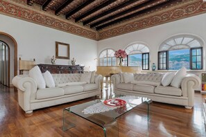 A spacious living room with two white sofas, a glass coffee table, and large arched windows offering a view of the outdoors. - Villa Schlosser Lake Front & Private Pool (Malcesine)