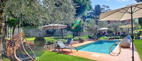 A backyard with a swimming pool, a hanging chair, and two lounge chairs.