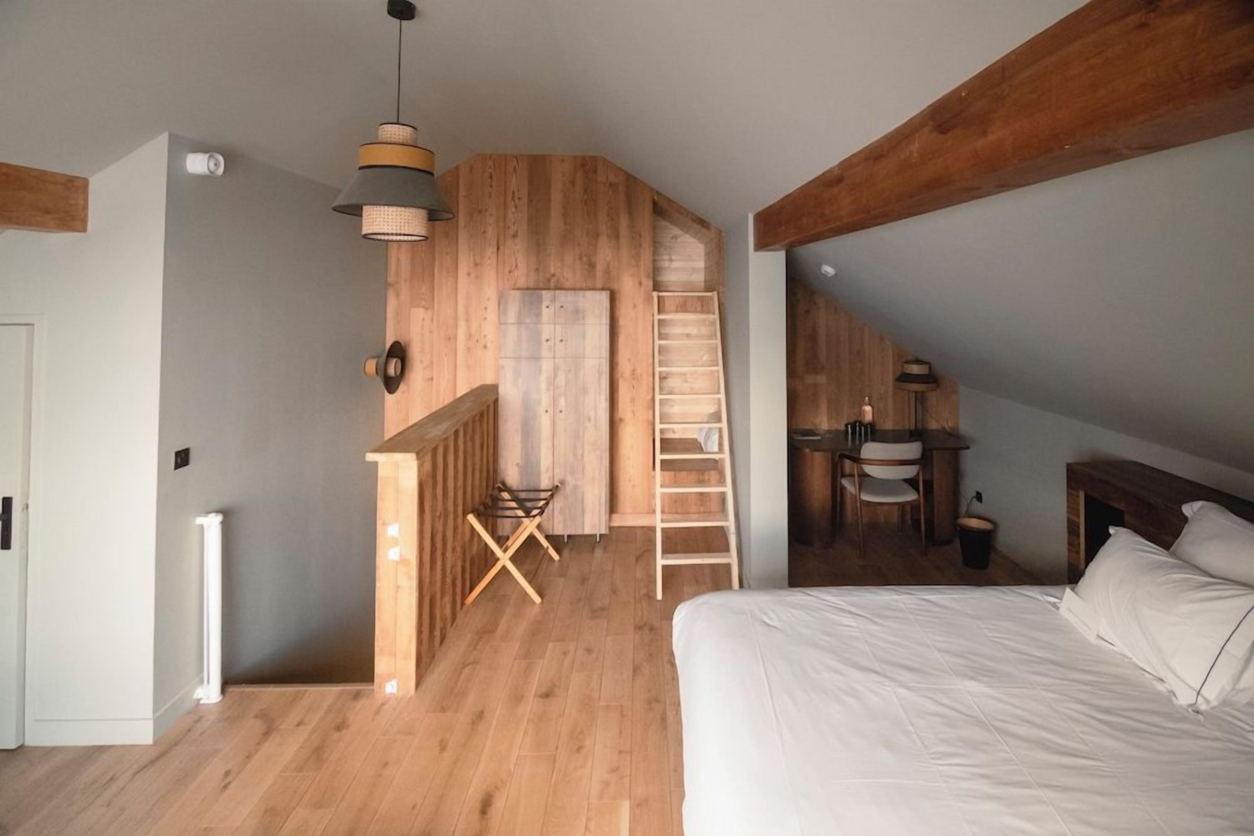Un dormitorio con techo de madera, una cama, un escritorio con una silla y una escalera.