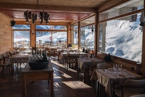Un restaurant au décor intérieur en bois, de grandes fenêtres offrant une vue sur les montagnes et des tables dressées pour le repas.