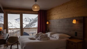Une chambre d’hôtel avec un lit, un bureau, une chaise, une table de chevet et une vue sur des montagnes enneigées.